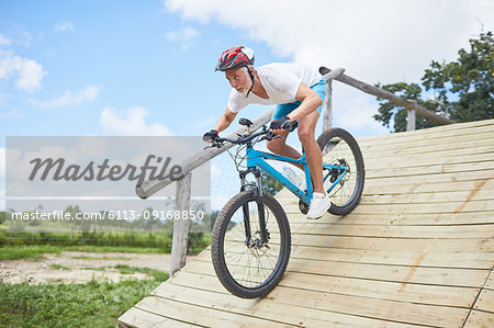 Focused mature man mountain biking down obstacle course ramp
