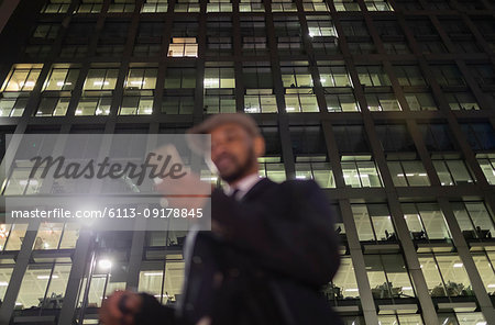 Businessman using smart phone below urban highrise at night