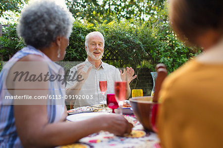 Senior friends enjoying lunch, talking at patio table