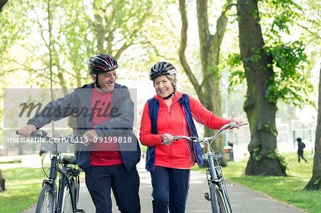 Active senior couple walking bikes in park