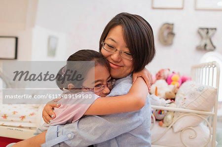 Affectionate mother and daughter hugging in bedroom