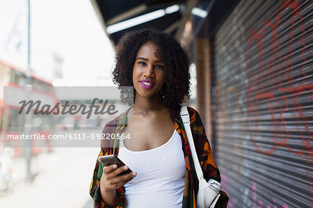 Portrait smiling, confident young woman with smart phone on urban sidewalk