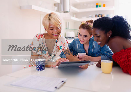 Young women friends drinking coffee and using digital tablet at kitchen table