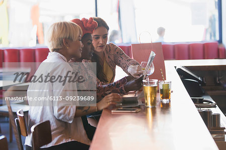 Young women friends looking at map, drinking cocktails in bar