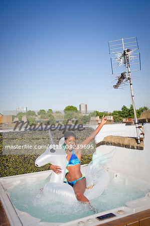 Portrait playful, carefree young woman in bikini on inflatable pegasus in sunny rooftop hot tub