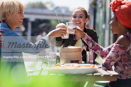 Young women friends toasting water glasses at dim sum lunch at sunny sidewalk cafe