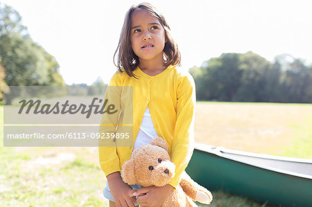 Girl with teddy bear in sunny field with canoe