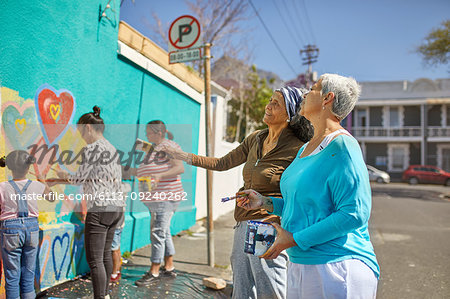 Community volunteers painting vibrant mural on sunny urban wall