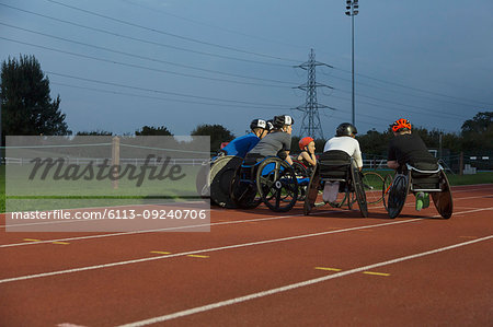 Paraplegic athletes huddling on sports track, training for wheelchair race at night