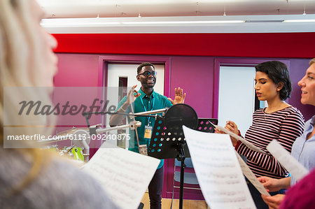 Male conductor leading womens choir with sheet music singing in music recording studio