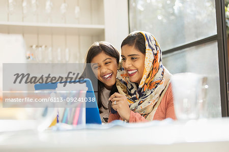 Happy mother in hijab and daughter using laptop