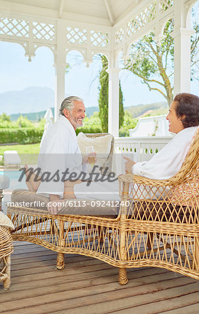 Mature couple in bathrobes relaxing, drinking champagne in resort gazebo