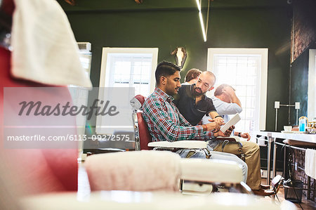 Male barber and customer with digital tablet talking in barbershop