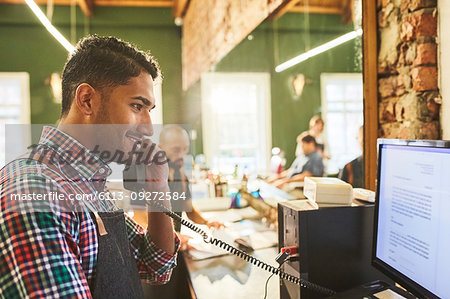 Male barber talking on telephone at computer in barbershop