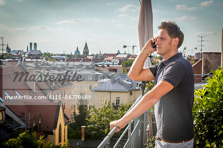 Man On Balcony Using Mobile Phone, Munich, Bavaria, Germany, Europe