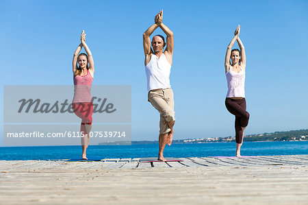 People practising yoga on a boardwalk, eagle pose