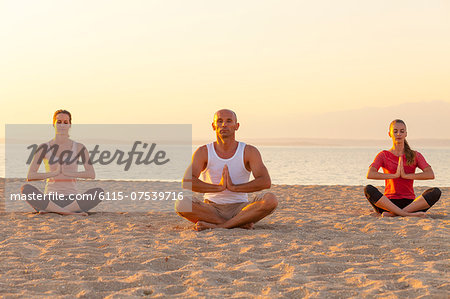 People practising yoga on beach, lotus pose