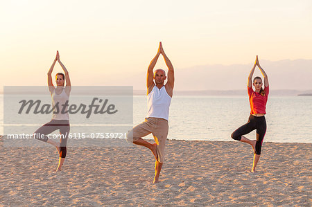 People practising yoga on beach, tree pose