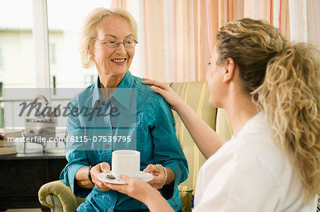 Senior woman receiving a cup of tea from nurse, Bavaria, Germany