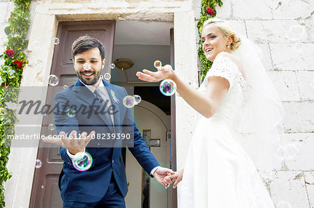 Bride and groom playing with soap bubbles in front of chapel