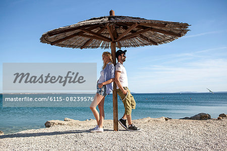 Young couple standing under parasol on beach