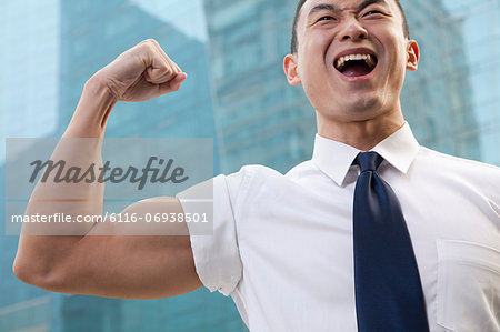Portrait of young businessman flexing muscle outdoors