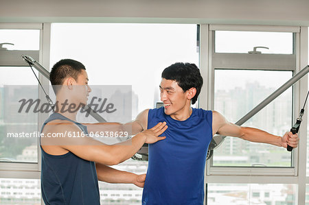 Young man exercising with his personal trainer in the gym