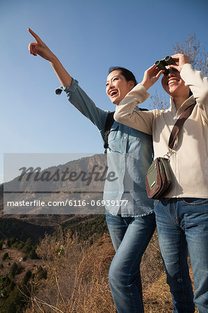 Women hiking, using binoculars, pointing at the mountain top