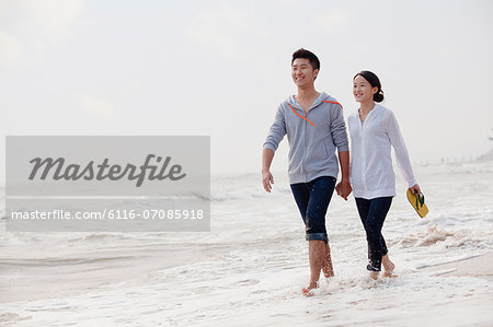 Young couple walking by the waters edge on the beach, China