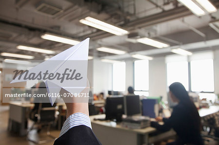 Hand holding paper airplane in office