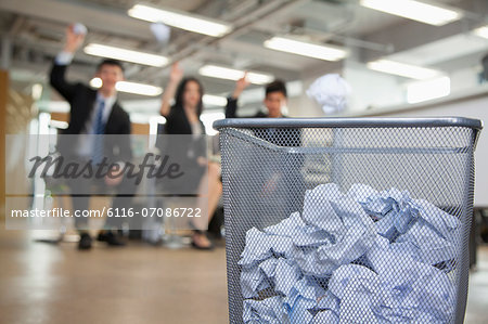 Three coworkers preparing to throw paper into waste basket
