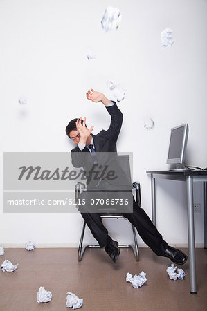 Young Businessman protecting himself from being hit by crumpled up pieces of paper