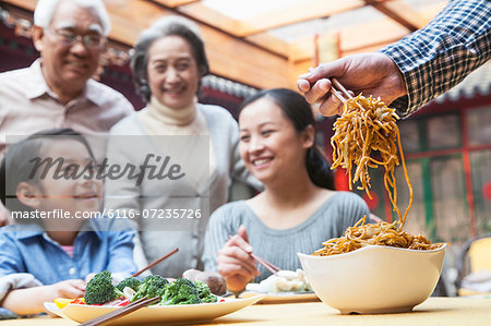 Father serving noodles with chopsticks at a family dinner