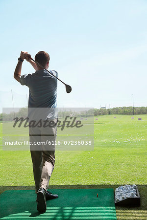 Rear view of young man hitting golf balls on the golf course, arms raised