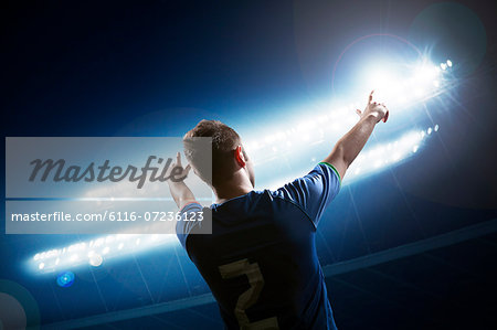 Soccer player with arms raised cheering, stadium at night time