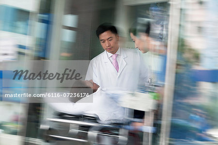 Two doctors wheeling in a patient on a stretcher through the doors of the hospital