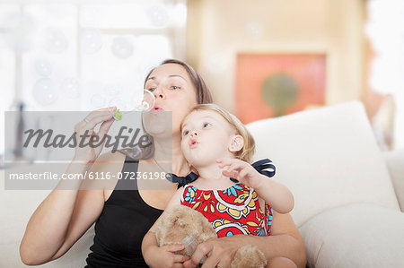 Mother and daughter sitting on the couch and blowing bubbles in the living room