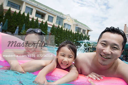 Smiling family portrait in the pool, father, mother, and daughter