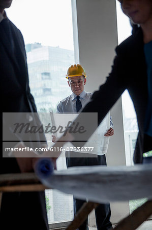 Three architects in hardhats examining blueprints in an office building