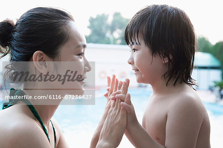 Smiling mother and son face to face and holding hands by the pool