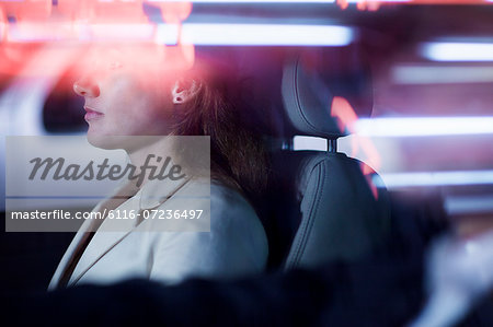 Serene businesswoman sitting in the car at night, illuminated and reflected lights on the car window