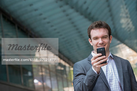 Summer. A Young Man In A Grey Suit And Blue Tie. Using A Smart Phone.