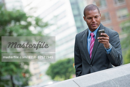 A Young Man In A Business Suit With A Blue Shirt And Red Tie. On A New York City Street. Using A Smart Phone.