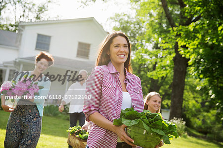 Family Party. Parents And Children Walking Across The Lawn Carrying Flowers, Fresh Picked Vegetables And Fruits. Preparing For A Party.