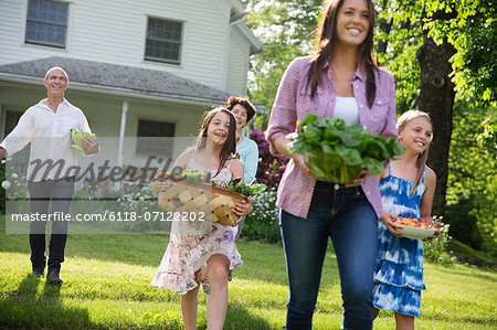 Family Party. Parents And Children Walking Across The Lawn Carrying Flowers, Fresh Picked Vegetables And Fruits. Preparing For A Party.