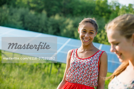 Two Young Girls On The Farm, Outdoors. A Large Solar Panel In The Field Behind Them.