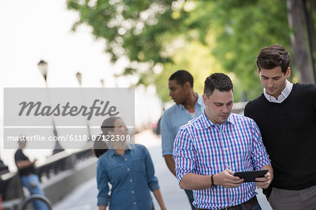 Summer In The City. Four People In A Group. One Using His Digital Tablet.