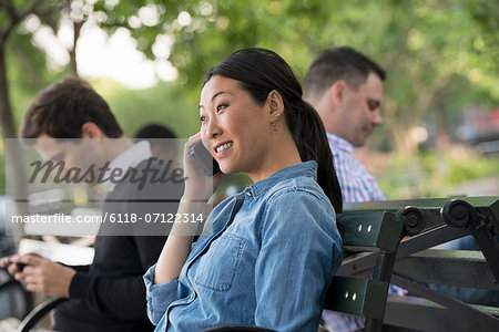 Summer In The City. One Woman And Three Men Sitting In The Park, Each On Their Own Phone Or Using A Tablet.