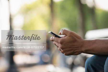 Summer. A Man Sitting On A Bench Using A Smart Phone.