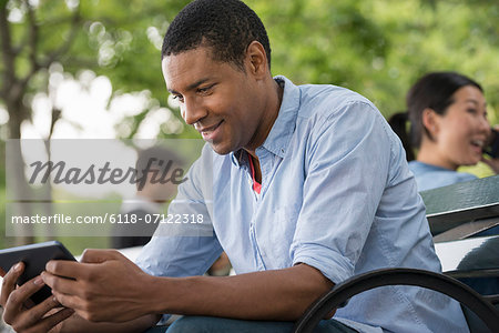 Summer. A Man Sitting On A Bench Using A Digital Tablet.